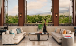 A woman traverses a lobby with grand bay windows looking out onto a green landscape